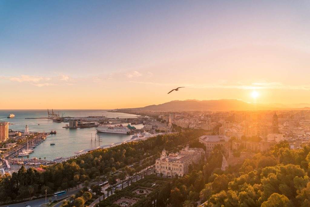 La ville s’illumine dans la douce lumière dorée du crépuscule. Un voilier plane au-dessus du port paisible.