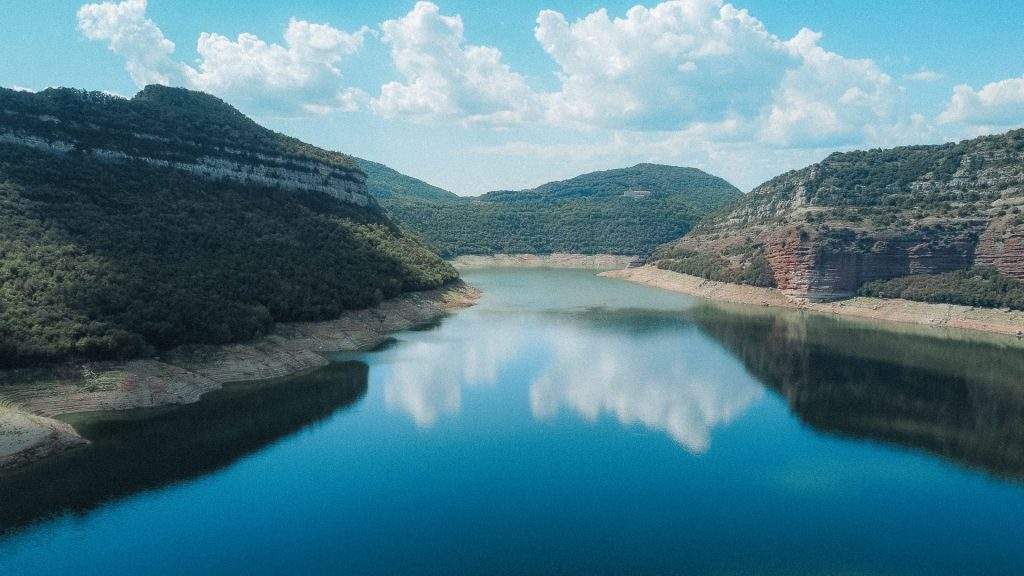 Réservoir bleu entouré de falaises boisées sous un ciel nuageux