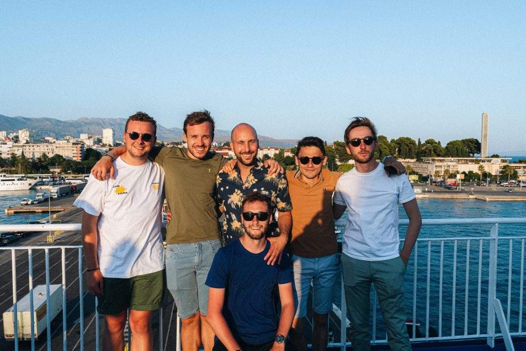 Six amis posent devant un port méditerranéen