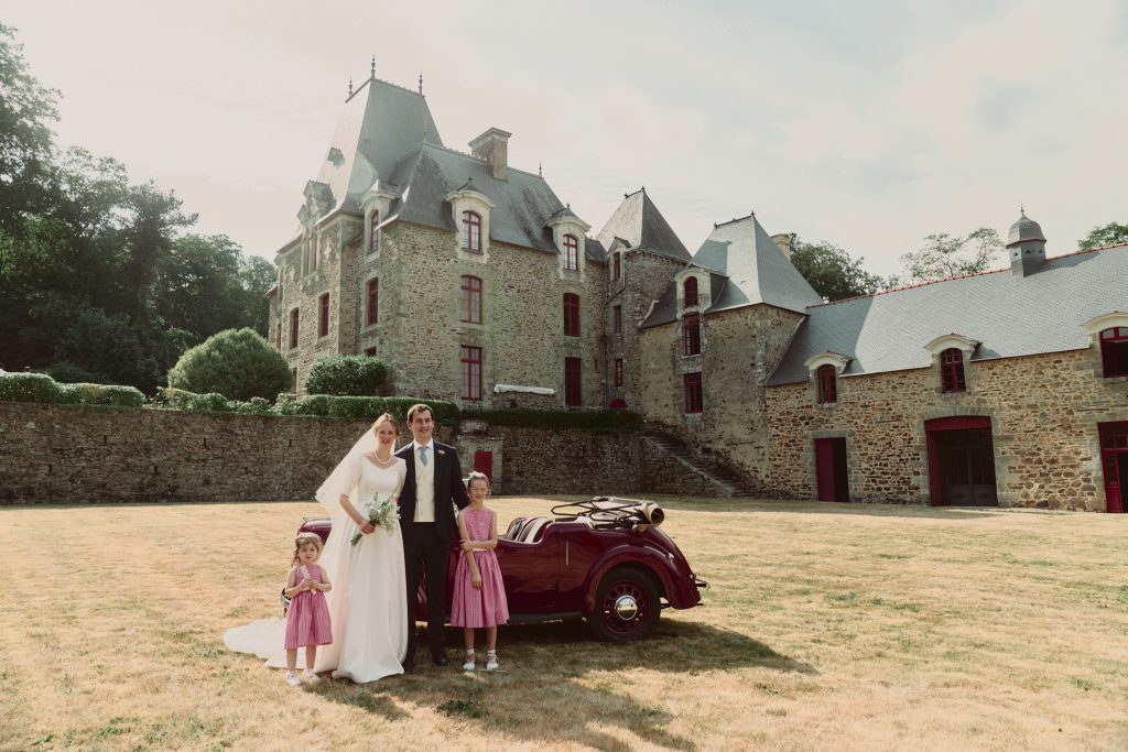 Mariés et enfants devant un château avec voiture ancienne