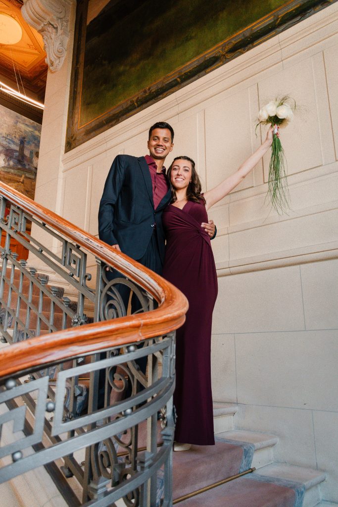 Couple souriant sur un escalier orné, bouquet à la main