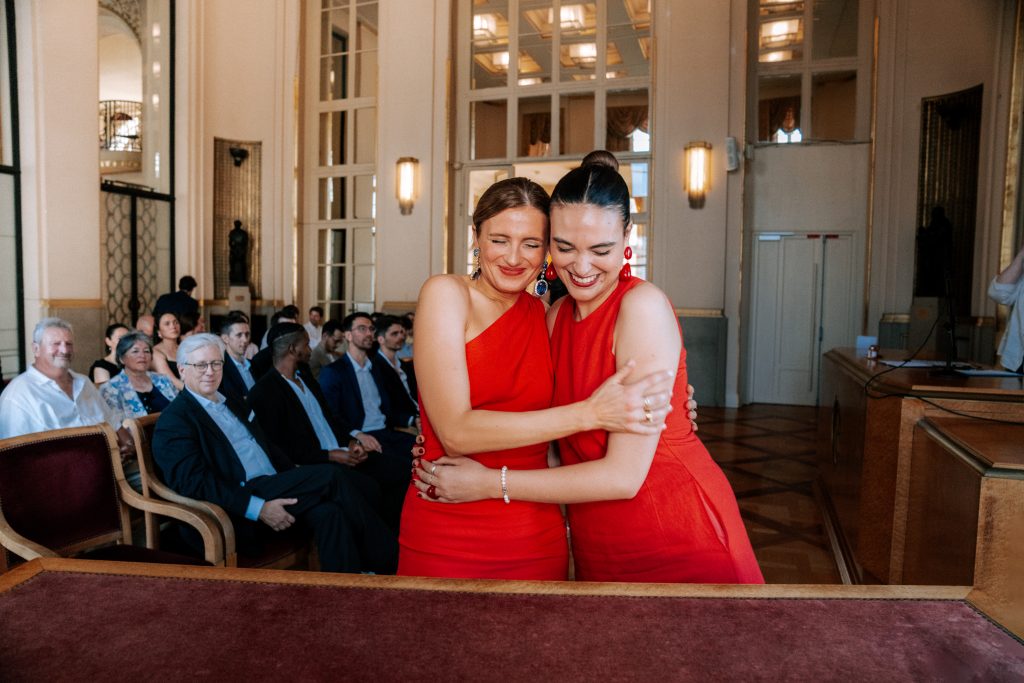 Deux femmes en rouge s’enlacent devant une assemblée