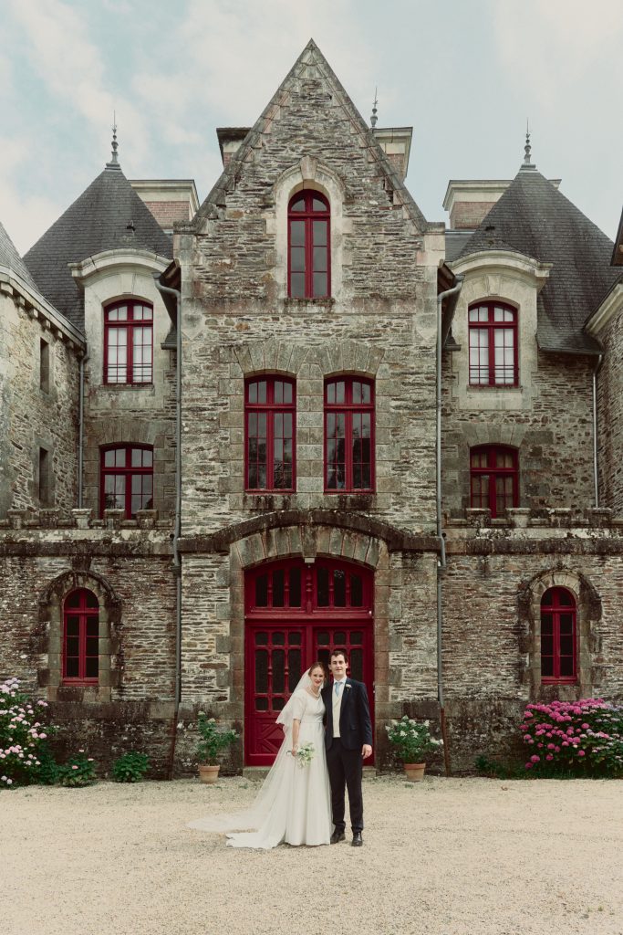 Mariés devant une chapelle en pierre aux portes rouges
